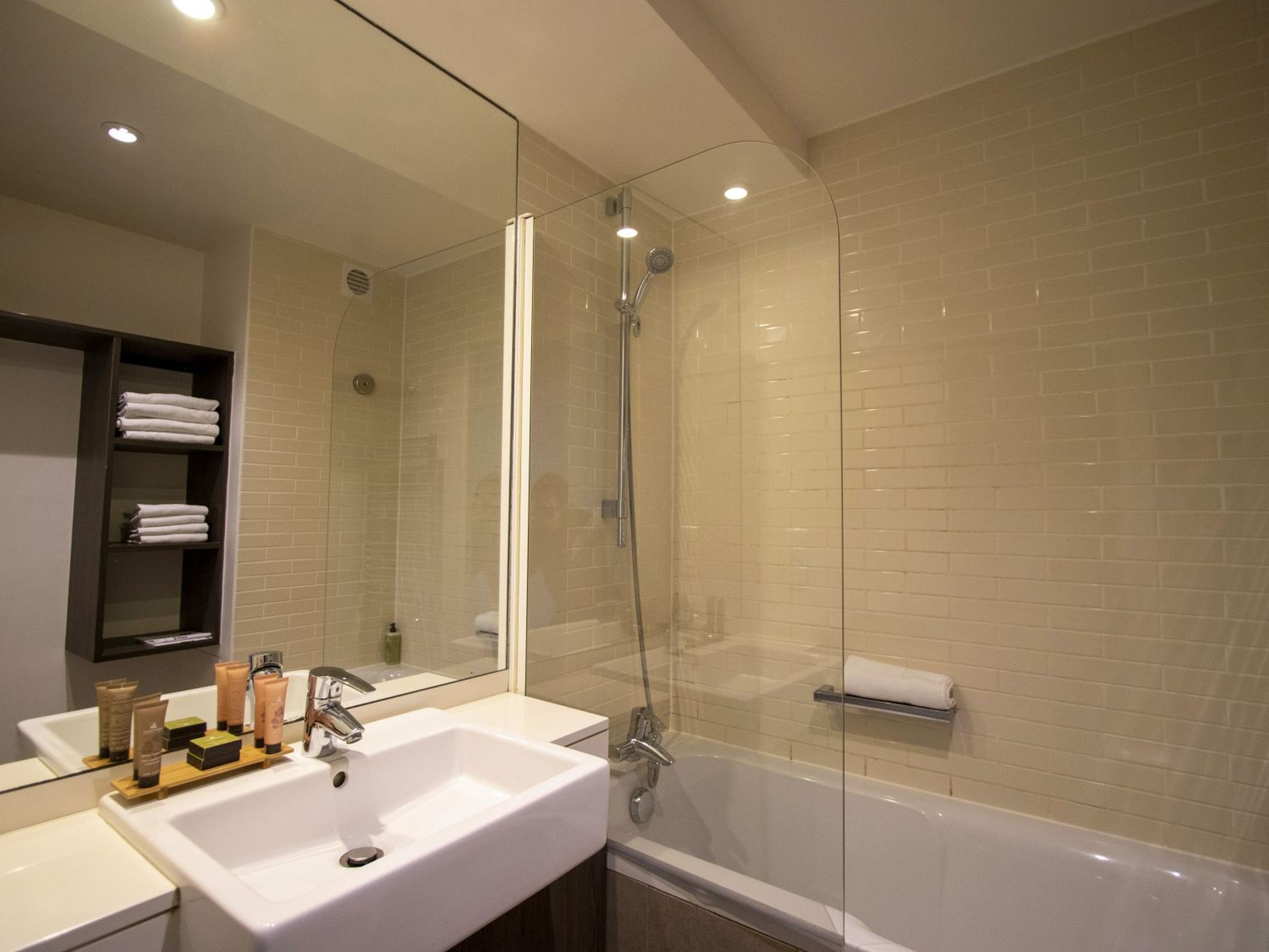 A modern bathroom with a glass-enclosed shower, a white sink with toiletries, and a towel rack.