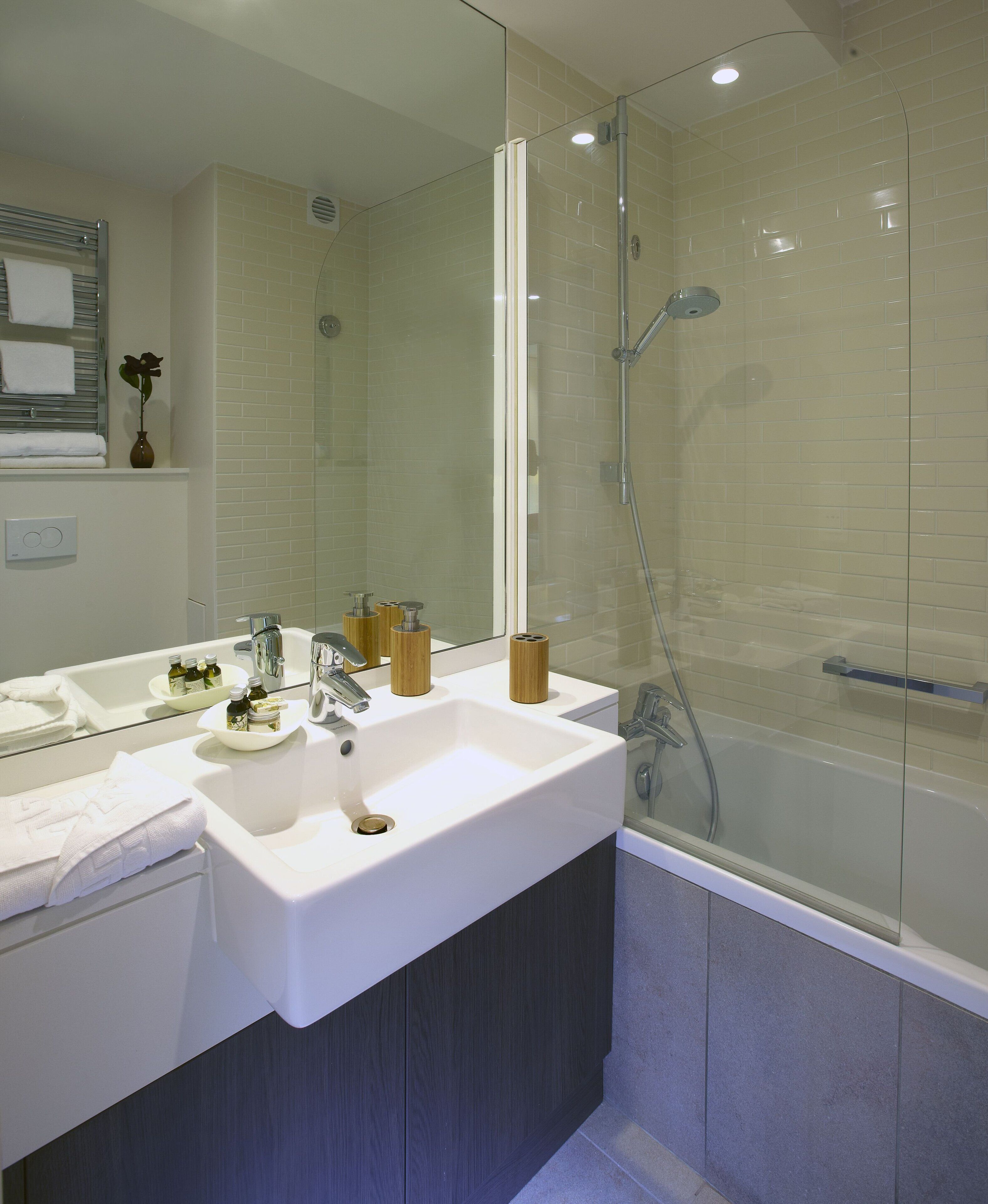 Un baño moderno con un espejo grande, un lavamanos blanco y una zona de ducha con mampara de vidrio.