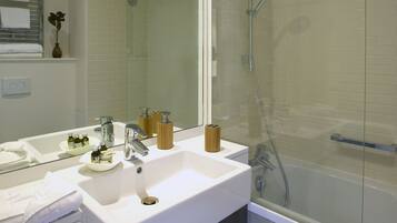 Un baño moderno con un espejo grande, un lavamanos blanco y una zona de ducha con mampara de vidrio.