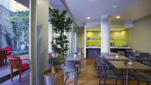 A restaurant with wooden tables and chairs, a bar area with a green counter, and a view of a garden with a large potted plant. - Citadines Montparnasse Paris (Paris)