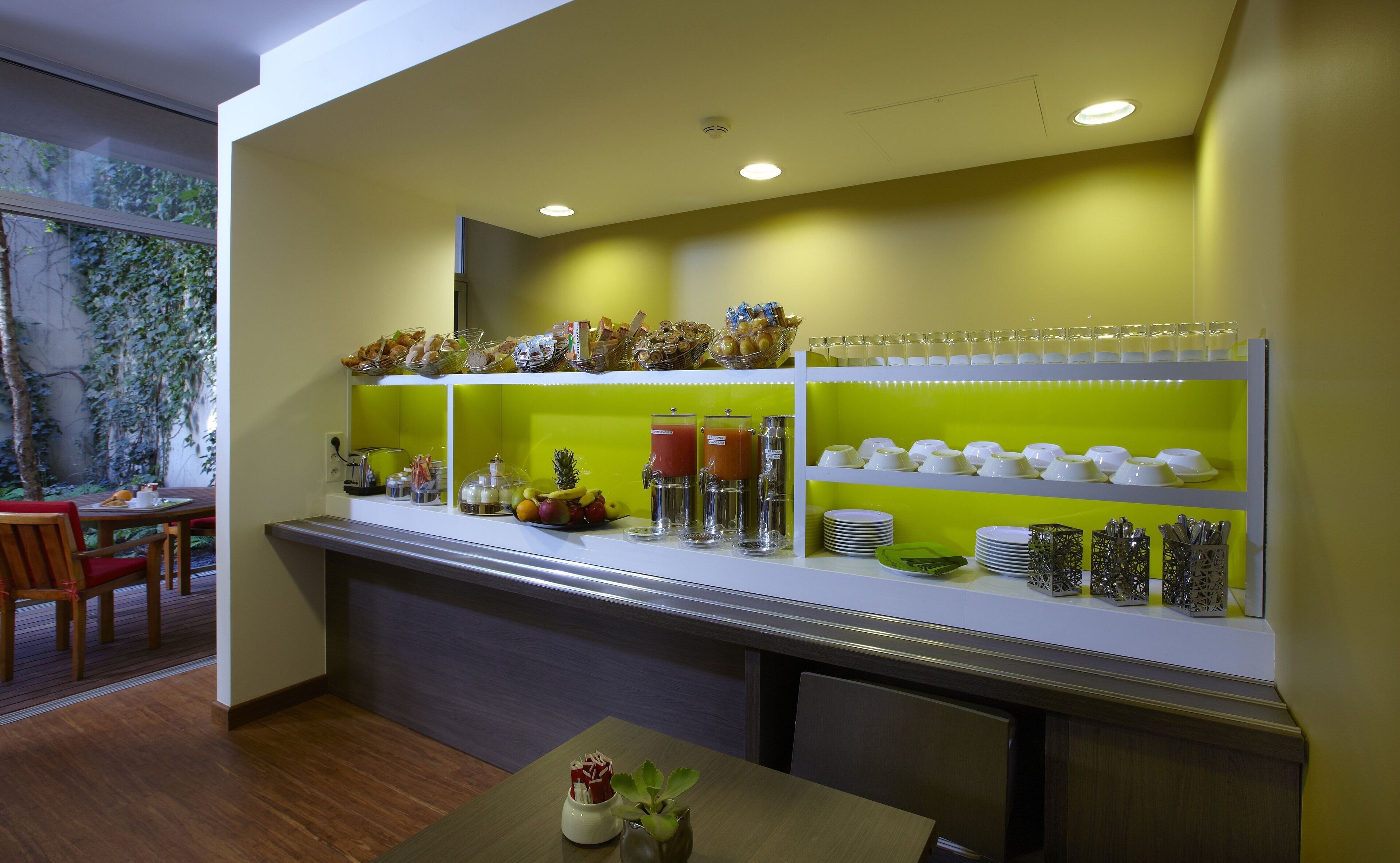 Un comptoir de petit-déjeuner proposant divers aliments et boissons, un espace détente avec une table et des chaises, et une vue sur la verdure environnante.