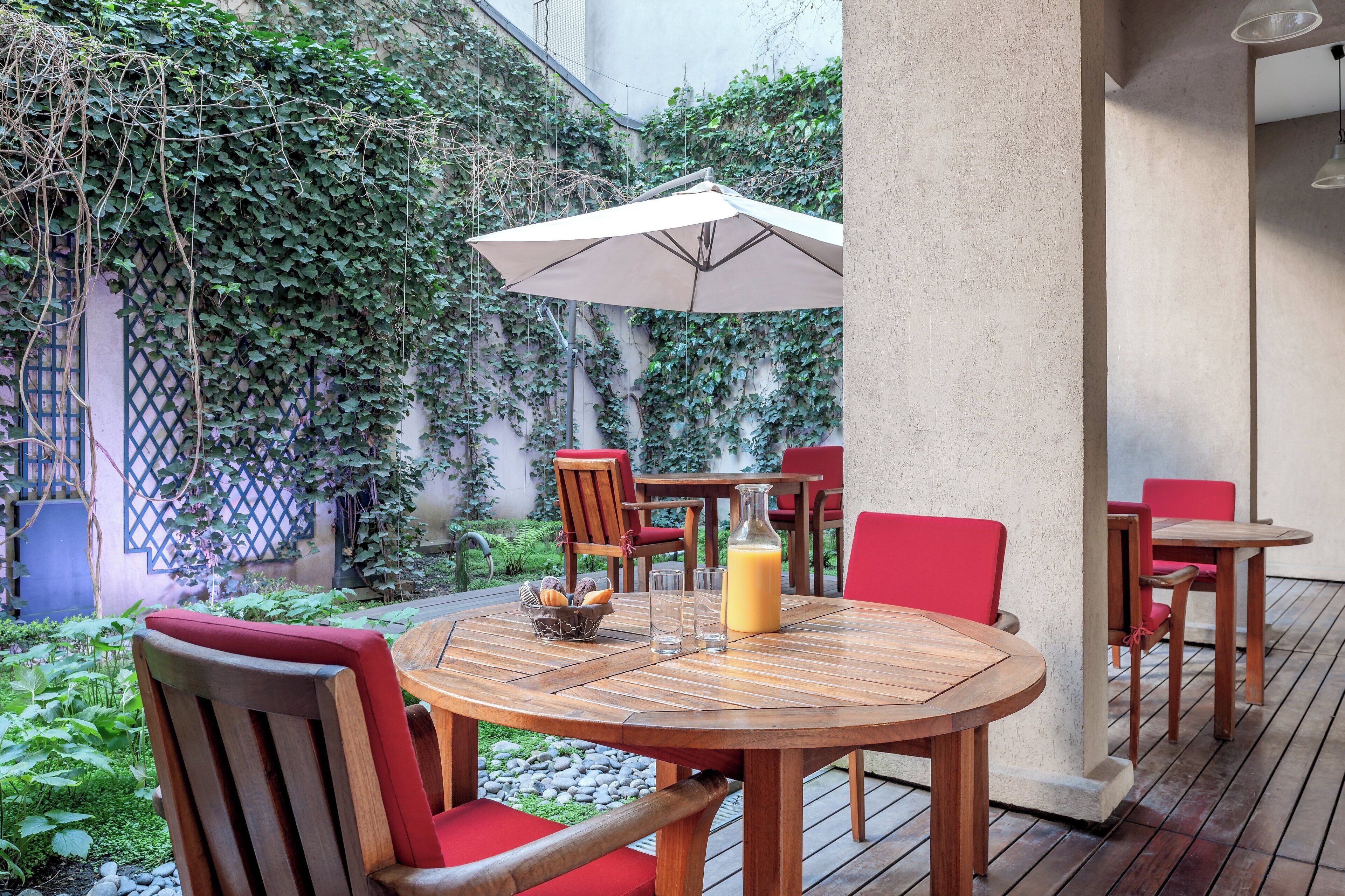 A wooden table with red chairs, an umbrella, and a glass of orange juice.