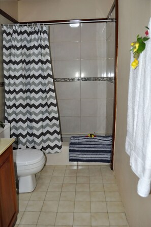 Un baño con cortina de ducha, inodoro, alfombra de baño a rayas y toallero con una toalla.