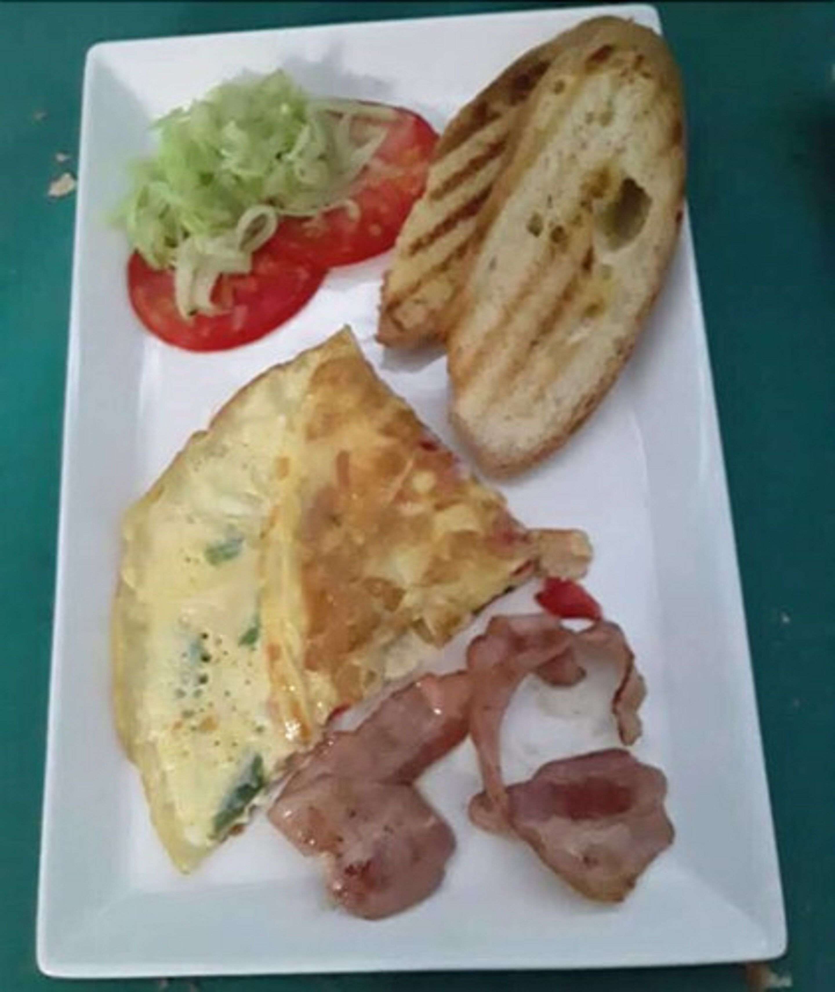 A plate with an omelette, bacon, grilled bread, and a side of salad.