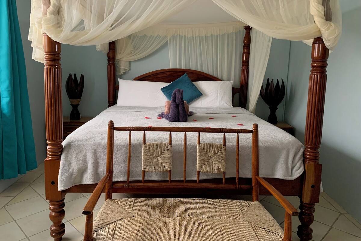 Una cama con dosel, una silla de mimbre y un cojín decorativo.