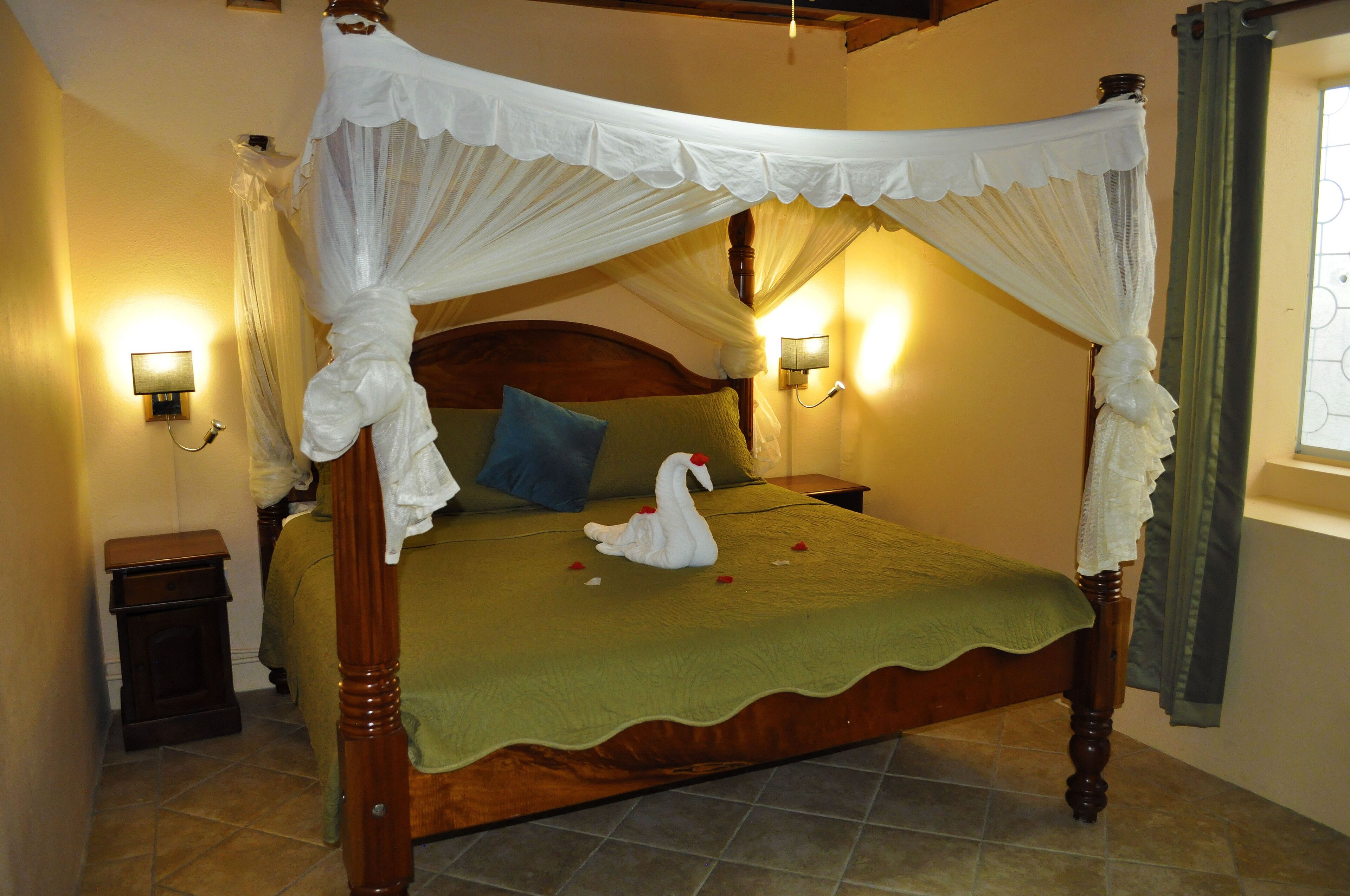 Una cama con dosel y cuatro columnas, con cubrecama verde, dos almohadas y una decoración de cisne blanco.