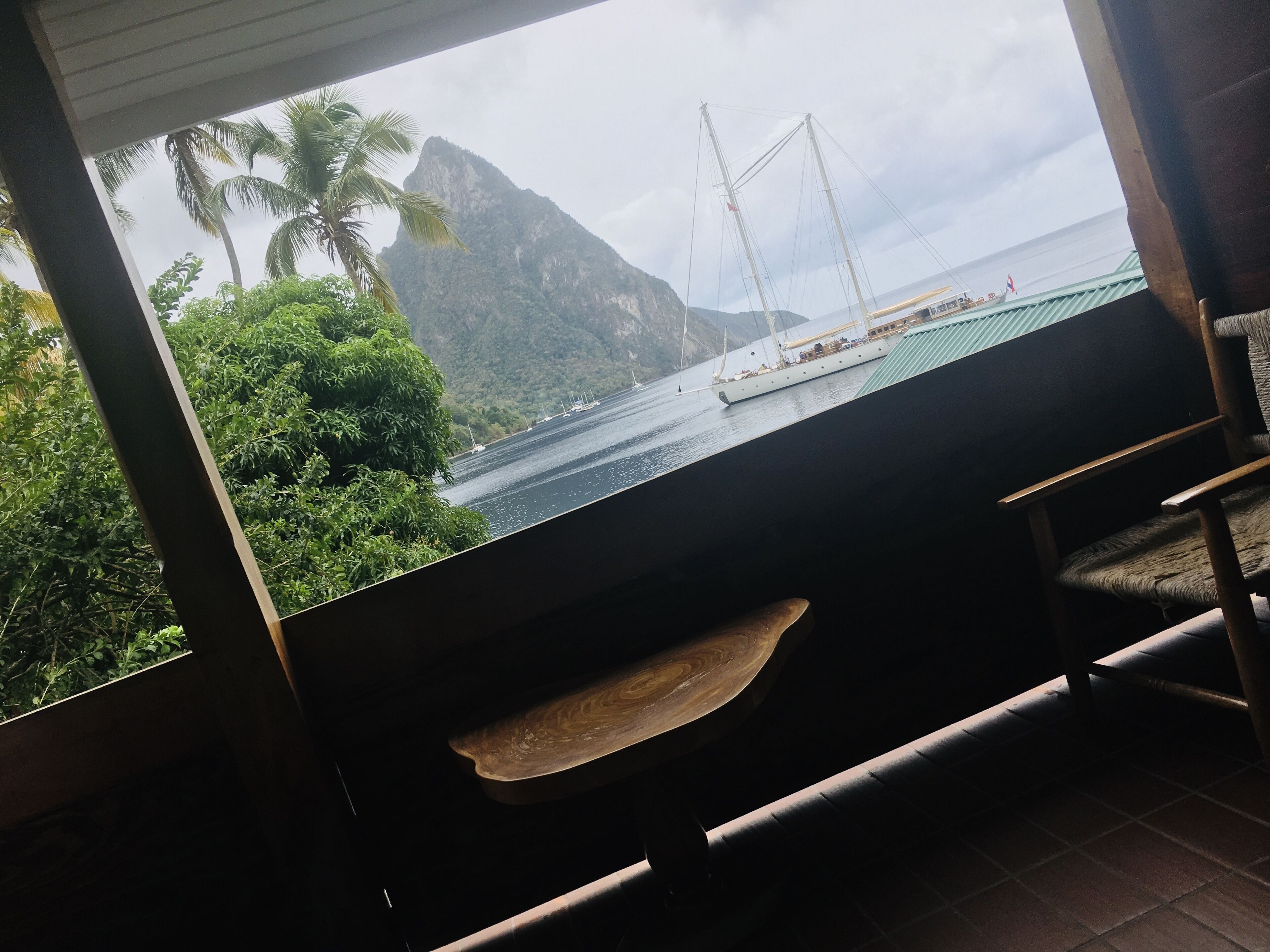 A view from a room with a large window overlooking a body of water, a sailboat, and a mountain.
