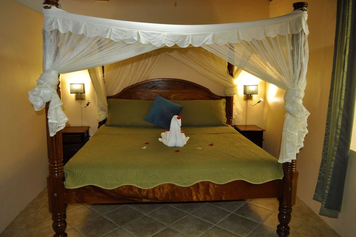 Una cama con dosel, colcha verde y almohada decorativa blanca.