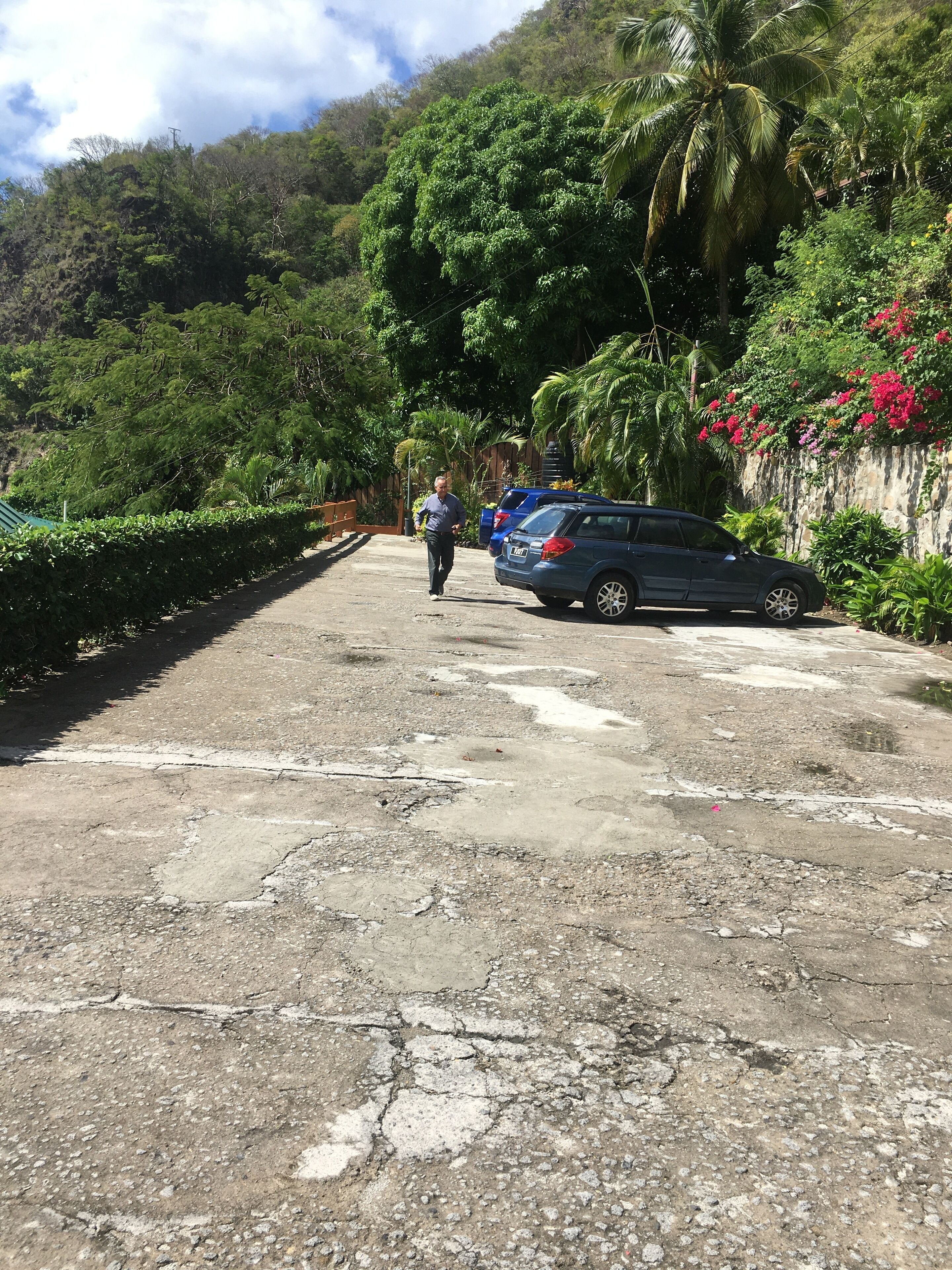 Ein Betonweg mit einem parkenden Auto auf der rechten Seite und einer weggestehenden Person.