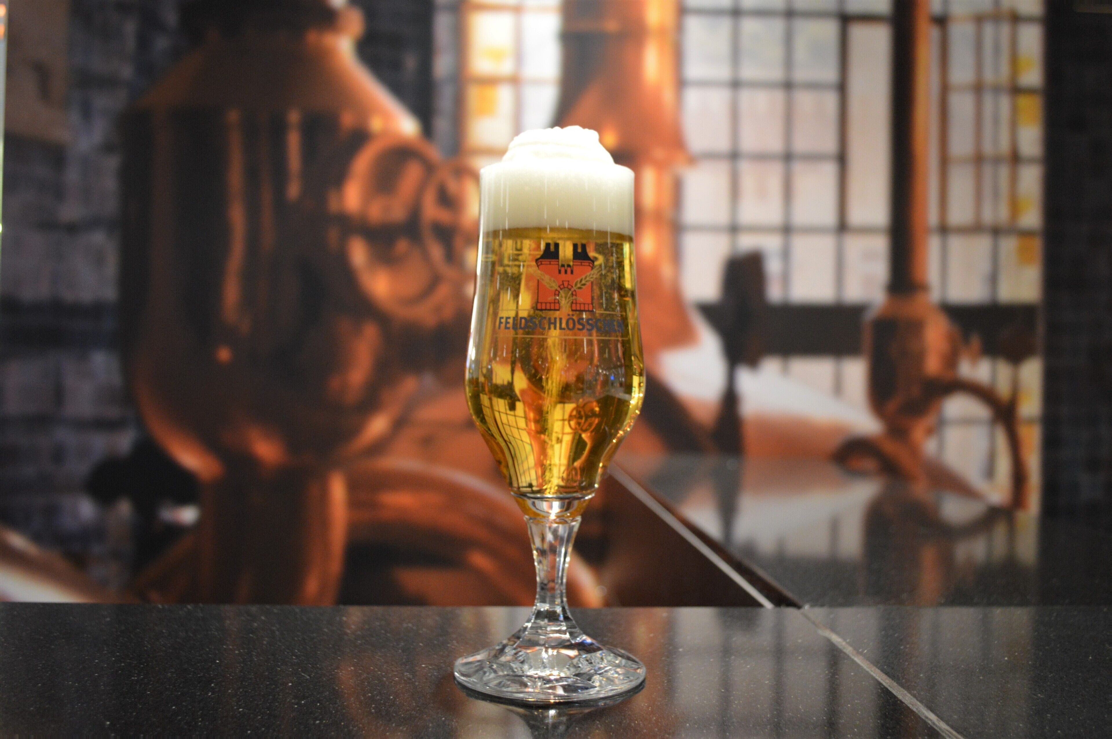 A glass of beer with a frothy head on a bar counter.