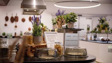A kitchen counter with jars of pasta, a sign reading "IN INSEPER Kueche," and various potted plants.
