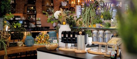 Una estación de café con una máquina de café, una vitrina de vidrio y una variedad de flores frescas.