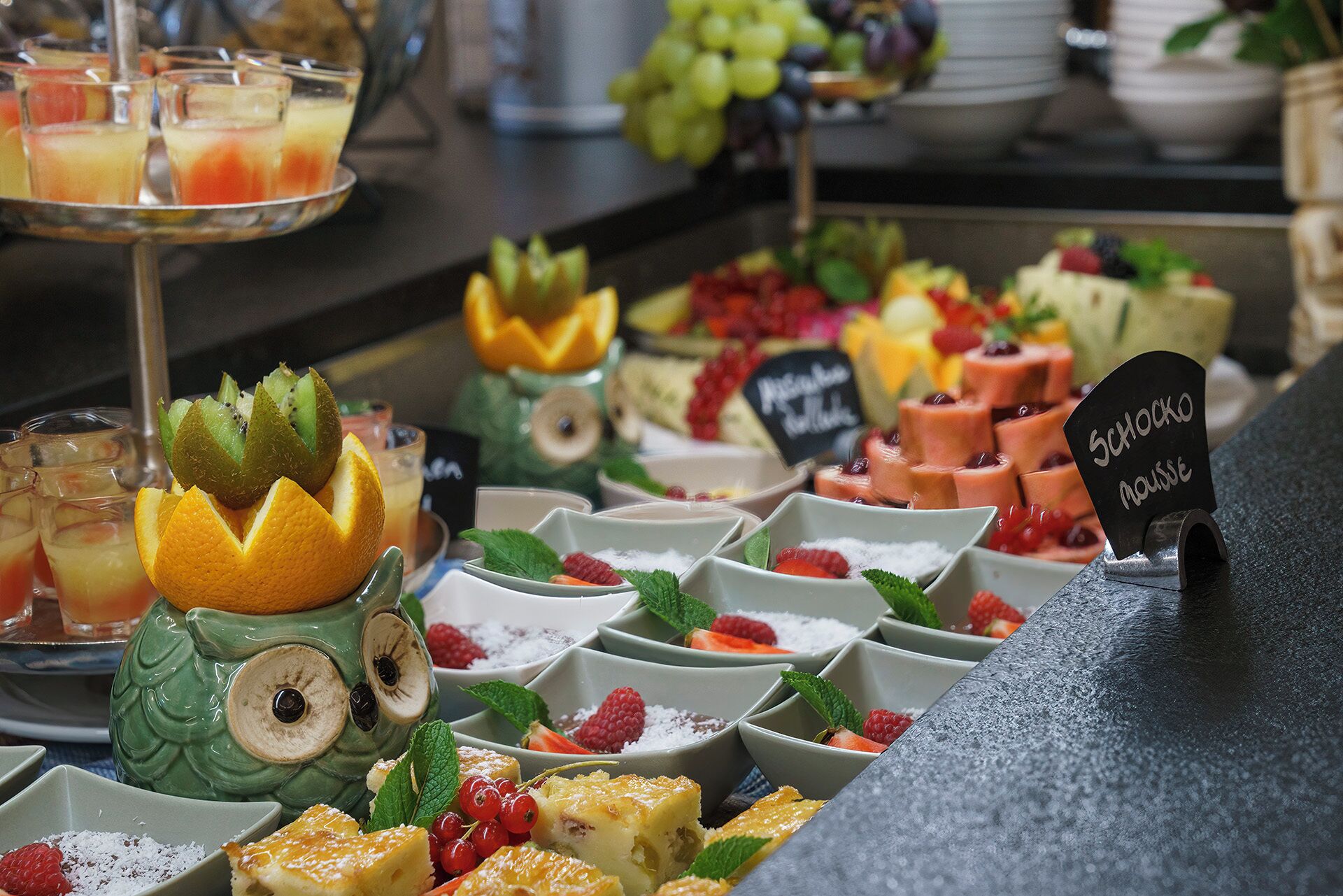 A buffet with various desserts and fruits, including a sign for 'Schocko Nausee'.