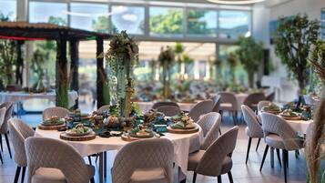 A spacious dining area with round tables set for a meal, surrounded by cushioned chairs.