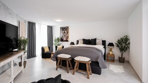 Un dormitorio moderno con una cama grande, dos taburetes, un televisor y una mesa de comedor.
