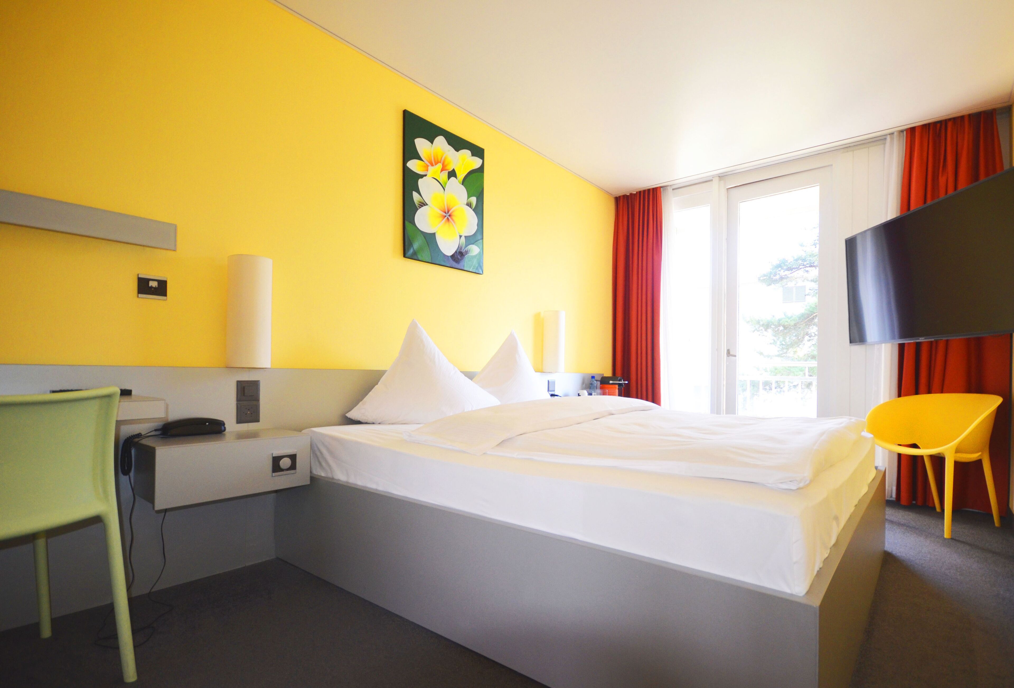 Habitación de hotel con cama, escritorio, silla, televisor y un cuadro en la pared.