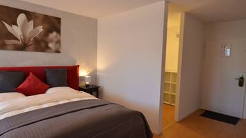 A hotel room with a bed, a nightstand, a lamp, and a door leading to another room.