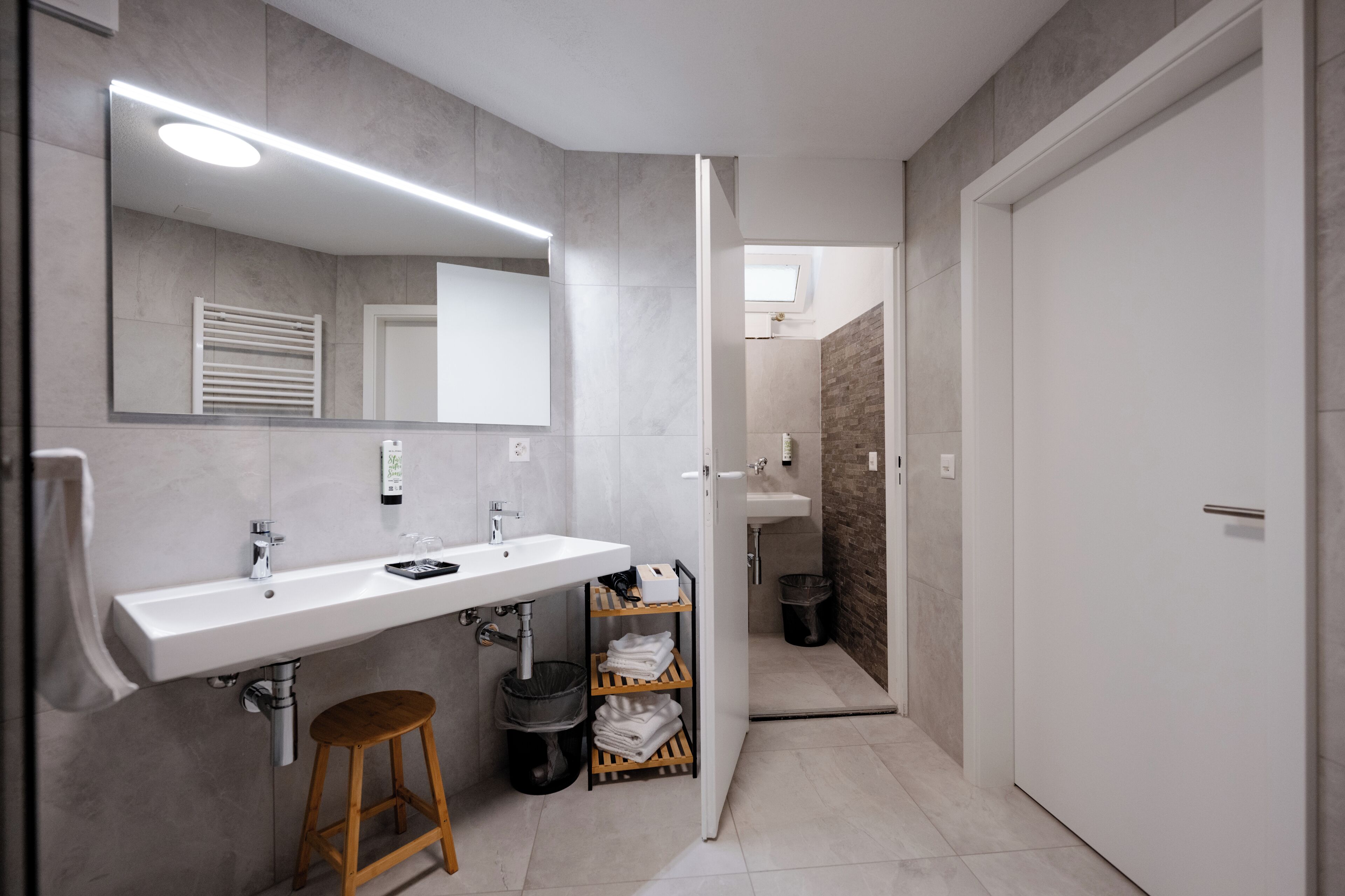 A modern bathroom with a white sink, mirror, and wooden stool.
