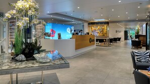 Un lobby de hotel moderno con mostrador de recepción, una mesa de vidrio con objetos decorativos y un área de descanso con mesas y sillas.
