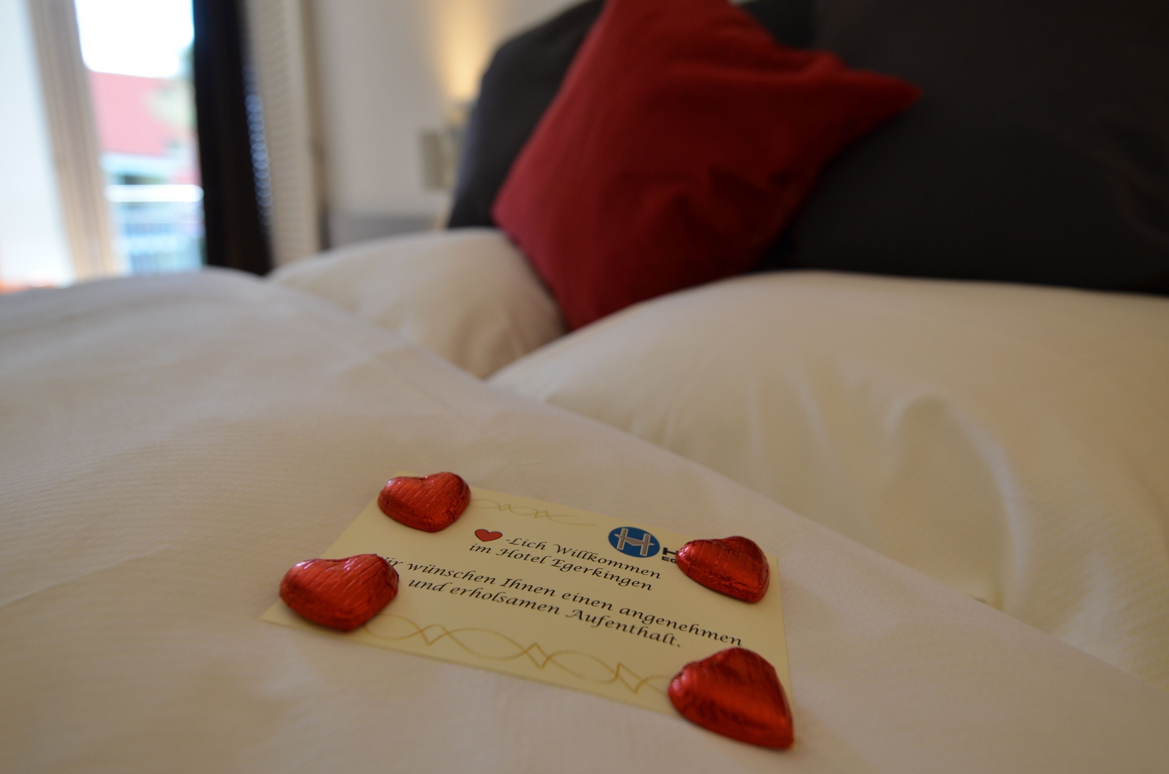 A bed with a note and heart-shaped chocolates.