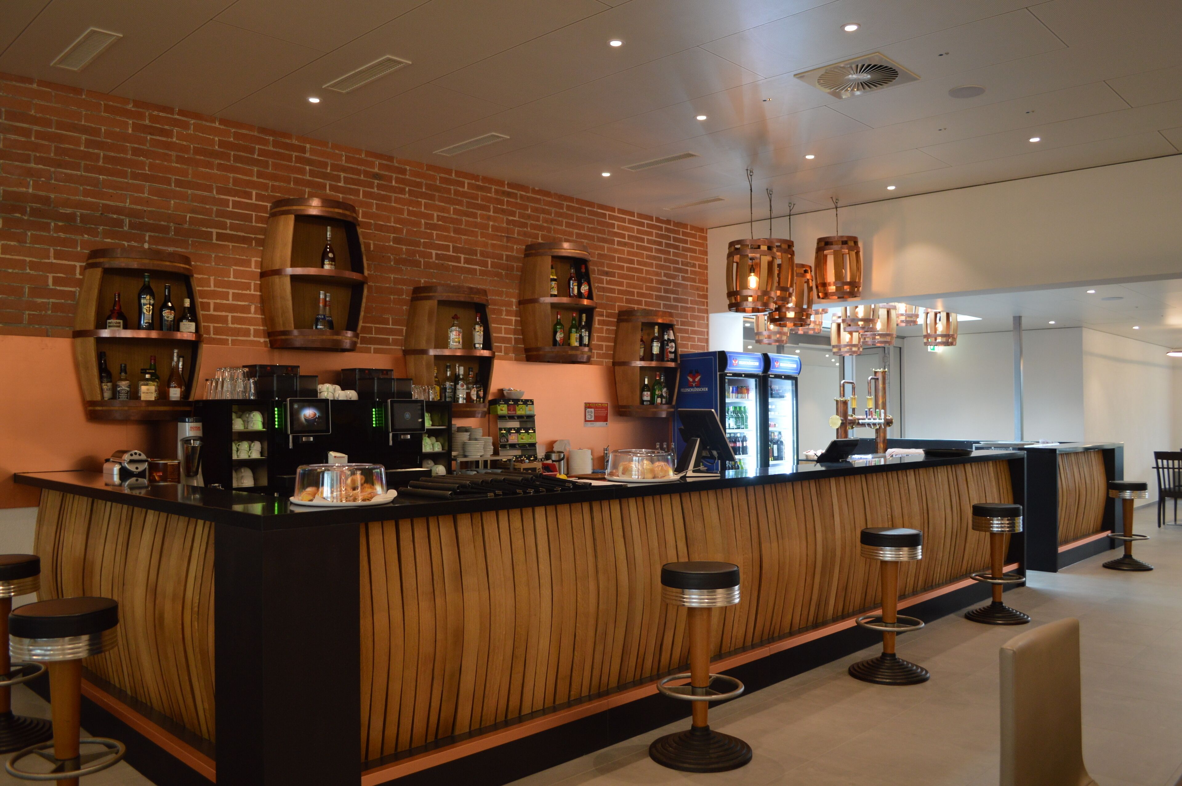 A bar area with wooden barrel shelves, a counter with stools, and a modern light fixture.