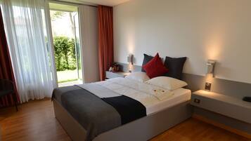 Ein modernes Hotelzimmer mit einem großen Bett, Nachttischen und Blick auf Grün durch das Fenster.