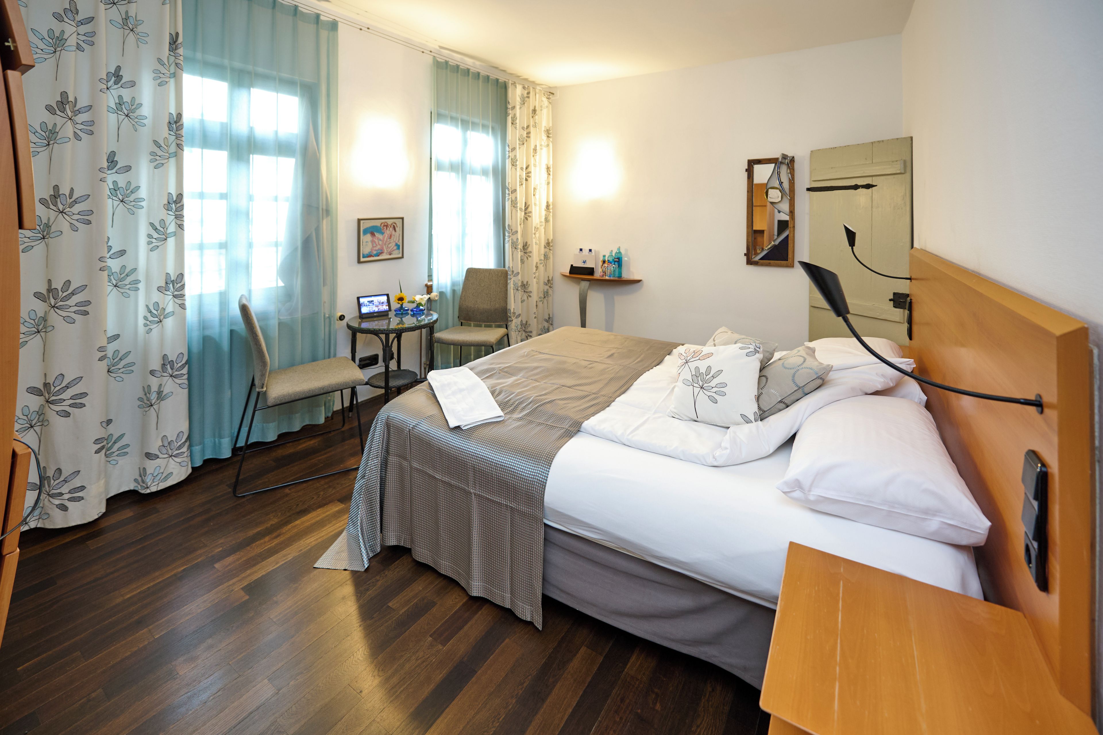 A hotel room with a bed, a chair, a small table, and a desk with a computer.