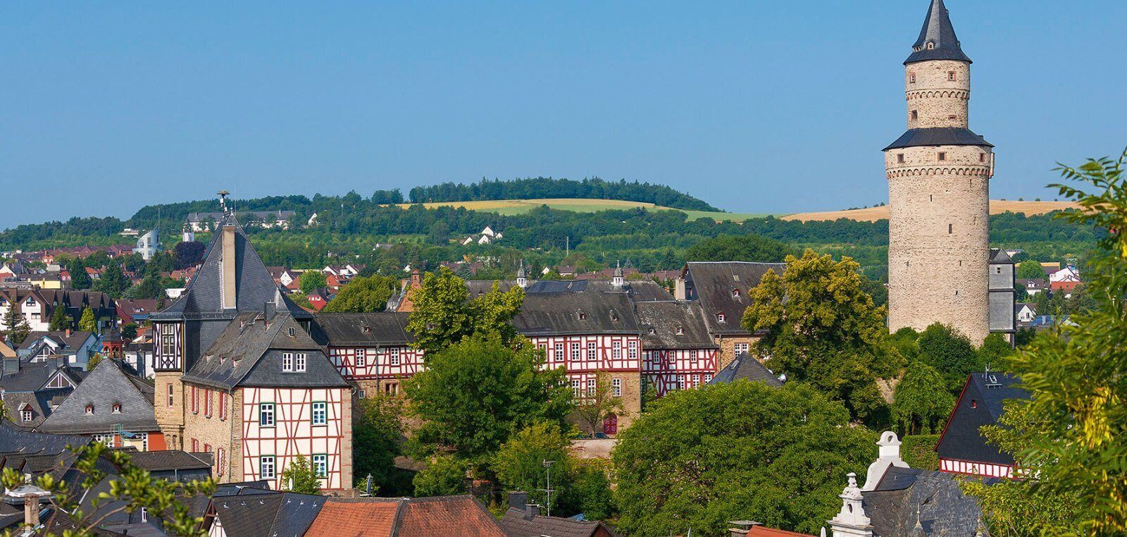 A town with traditional half-timbered houses, a prominent tower, and a hill in the background.