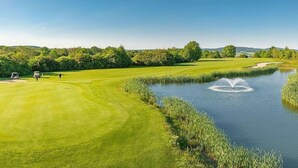 Un campo de golf con un estanque, árboles y cielo despejado.