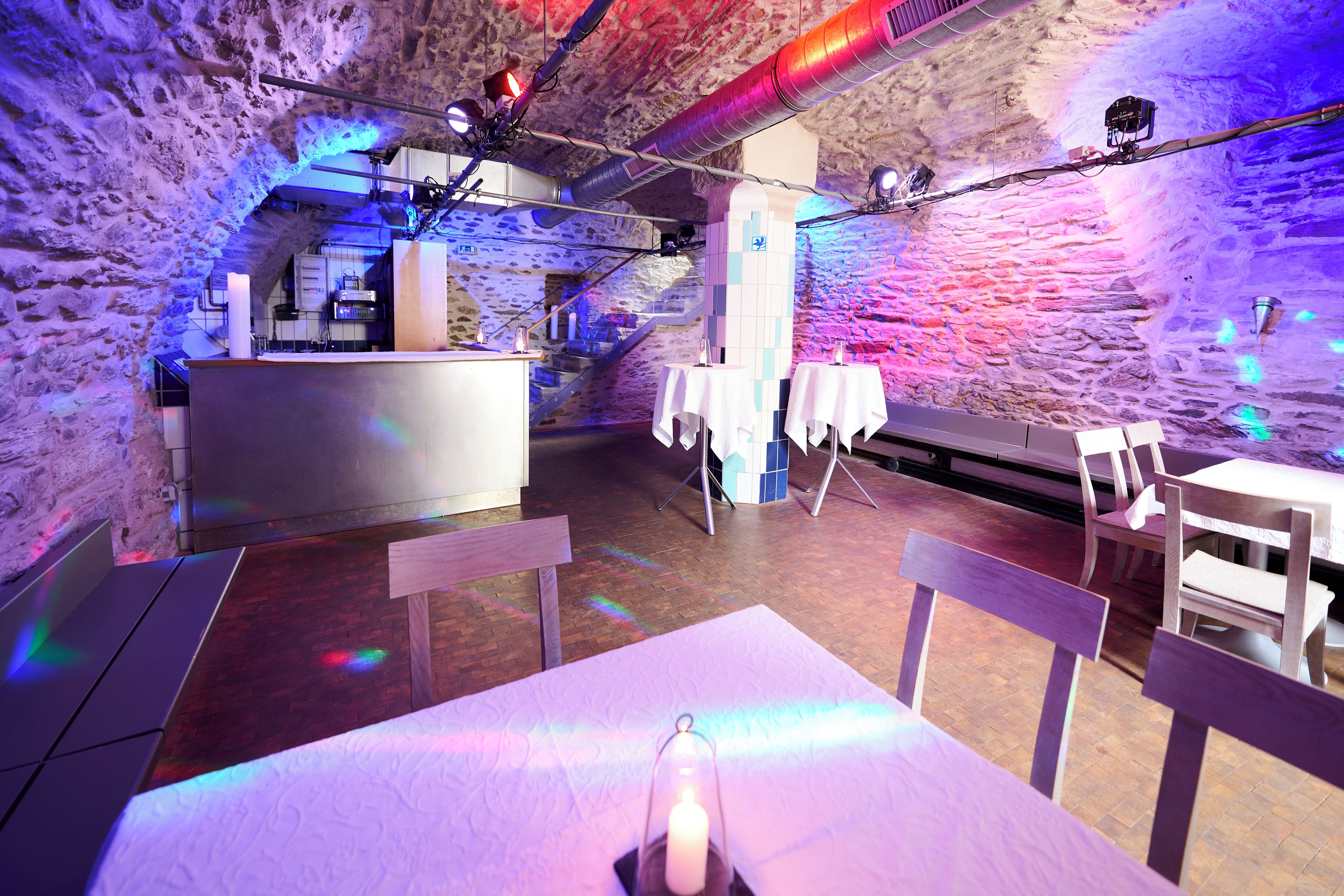 An interior with stone walls, a bar area, tables with chairs, and a staircase.