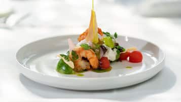 A white plate with a seafood dish, including shrimp and vegetables, and a drizzle of sauce.