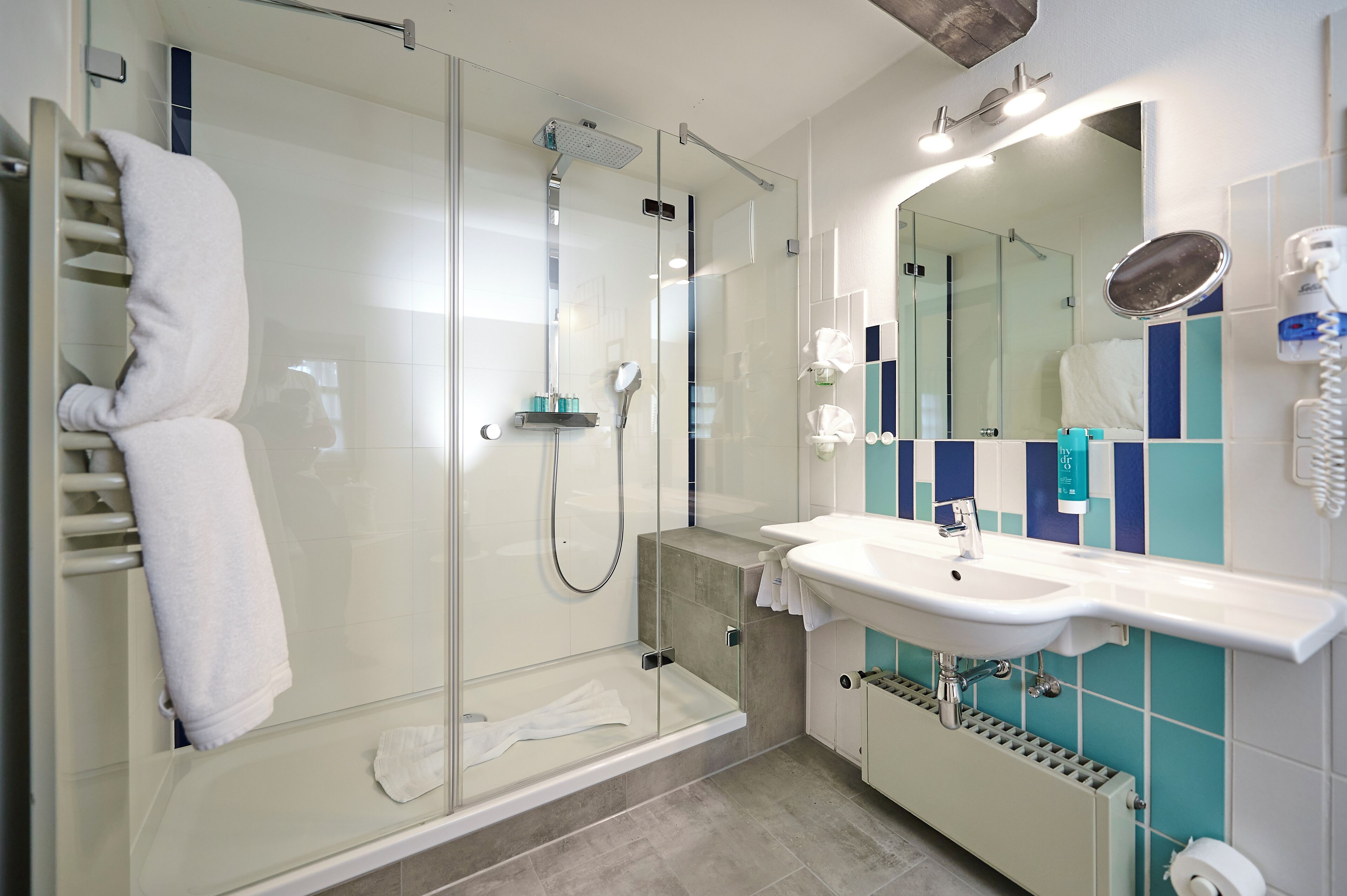 A modern bathroom with a glass-enclosed shower, a white sink, and a mirror with a telephone.
