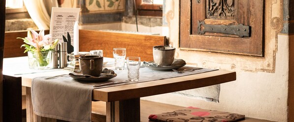 Una mesa de madera con mantel, un florero con flores, una vela, un menú y una pared rústica con una puerta.