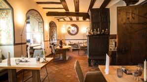 Un restaurante acogedor con decoración rústica, que presenta vigas de madera a la vista, un ventanal con vitrales y un aparador de madera tradicional.