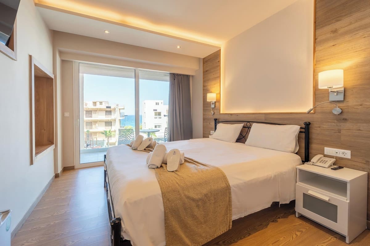 A hotel room with a large bed, a bedside table with a phone, and a view of the city through the window.