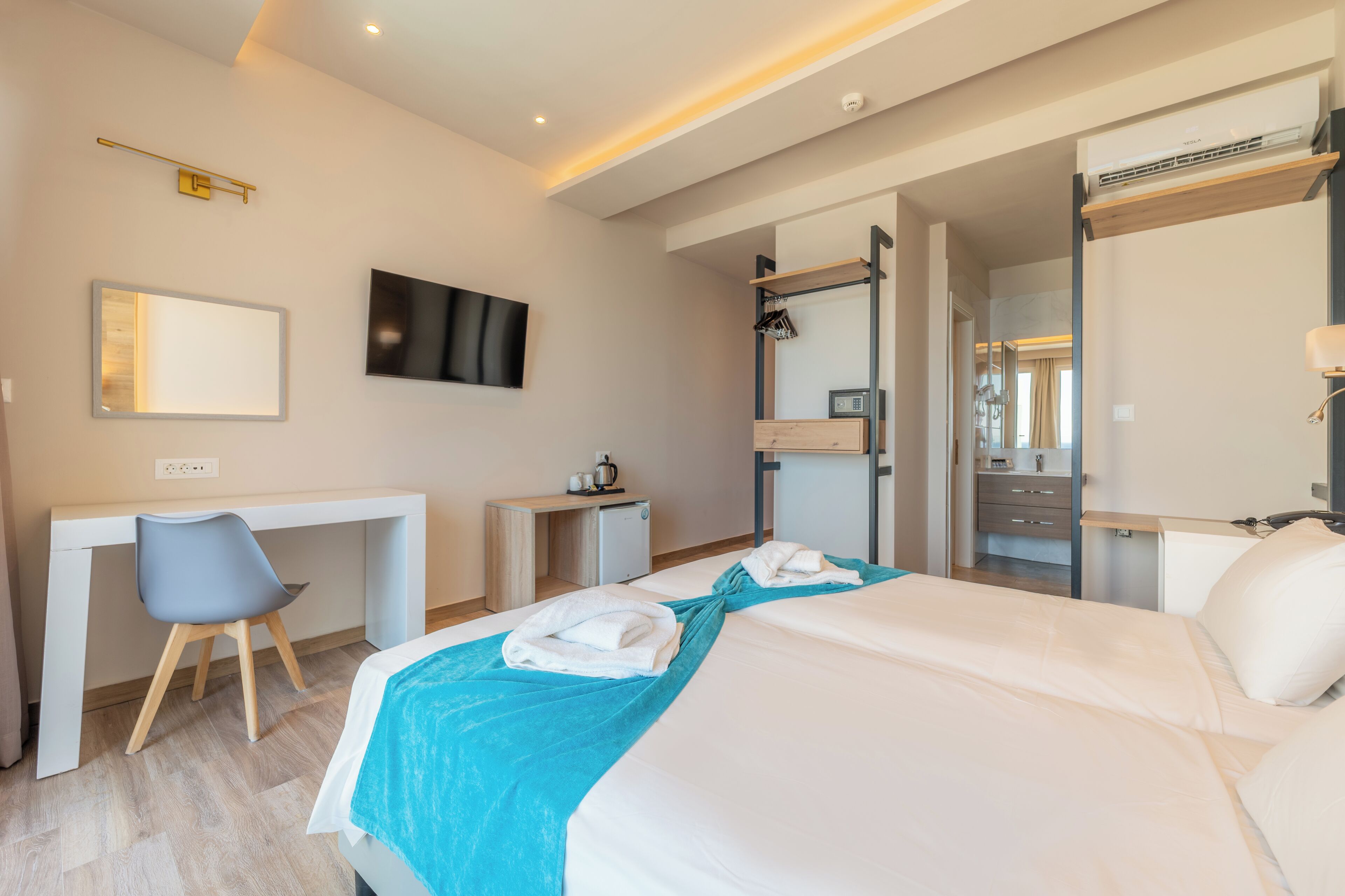 Ein modernes Hotelzimmer mit Bett, Schreibtisch, Sessel und einem an der Wand befestigten Fernseher.