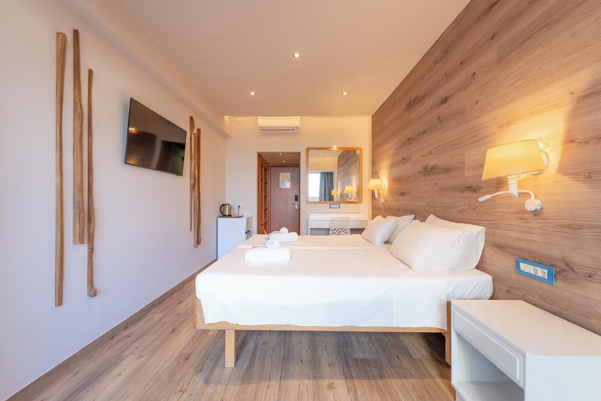 Une chambre d’hôtel comprenant un lit, une table de chevet, un miroir, une lampe fixée au mur et un mur décoratif en bois.