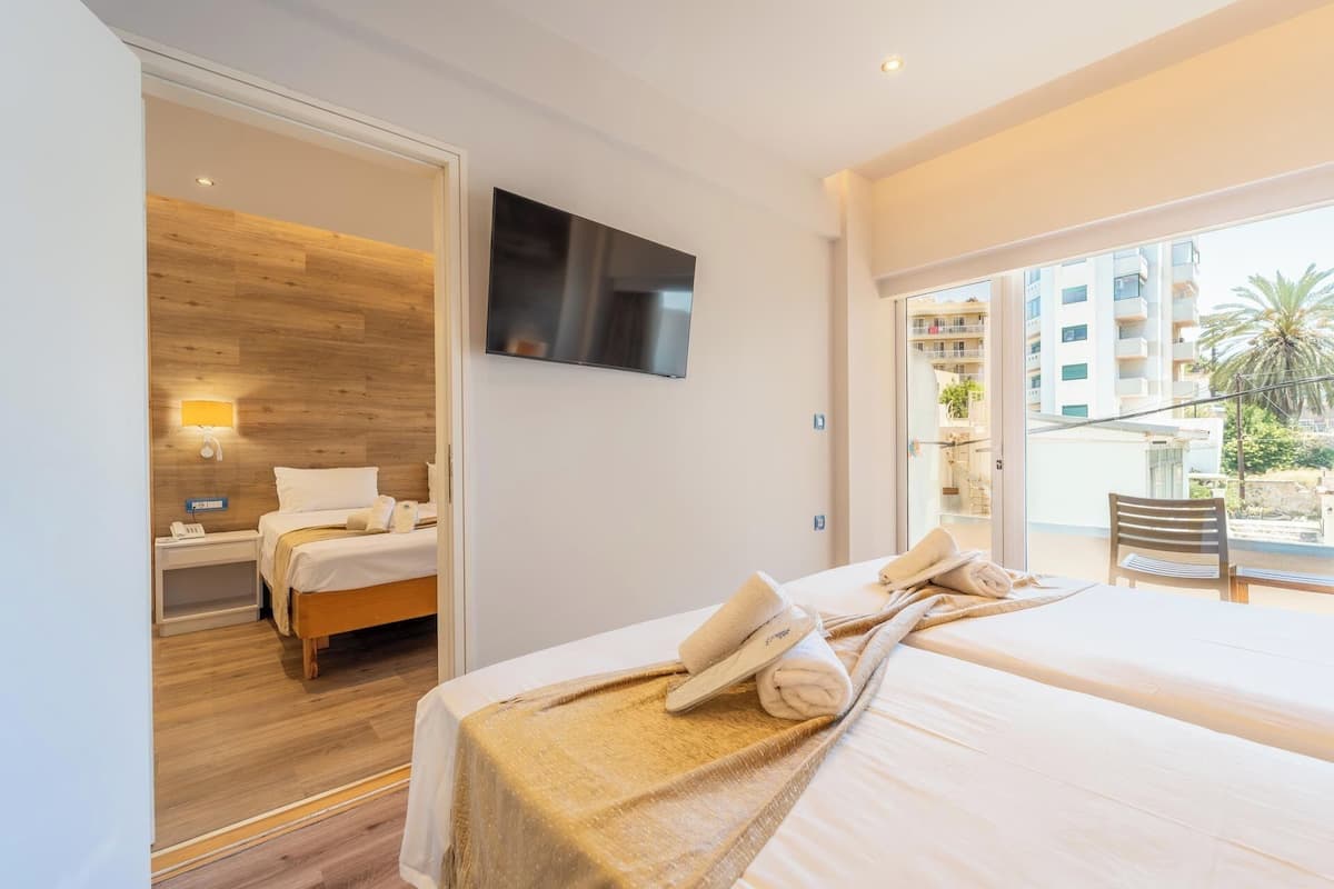 A hotel room with a bed, a TV, a nightstand, a lamp, and a view of the outside balcony.