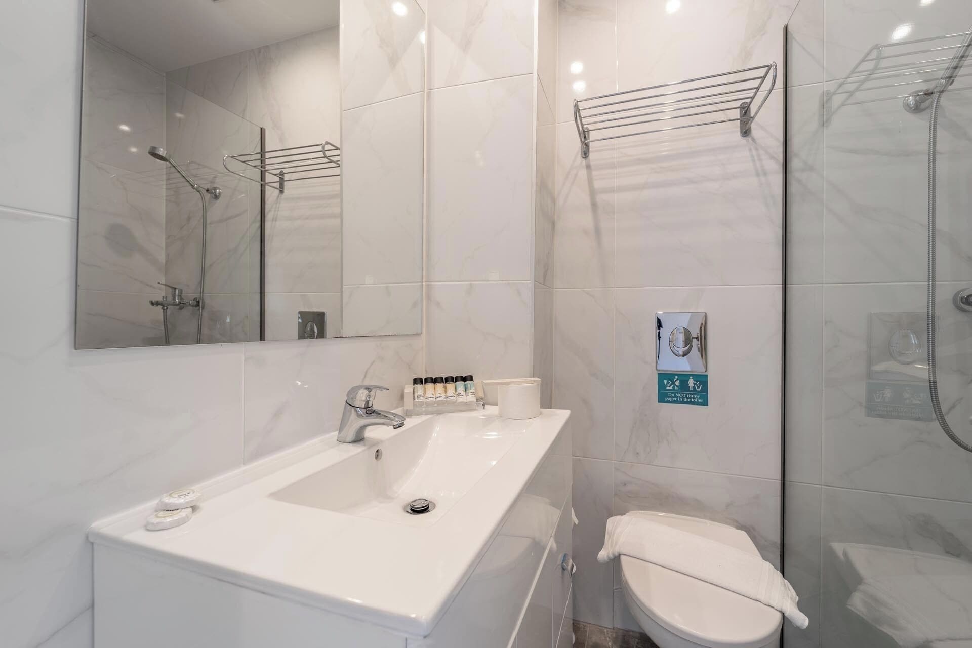 Een moderne badkamer met een wit wastafelmeubel, spiegel en toilet. Er is een douchegedeelte met een glazen deur en een handdoekhouder.