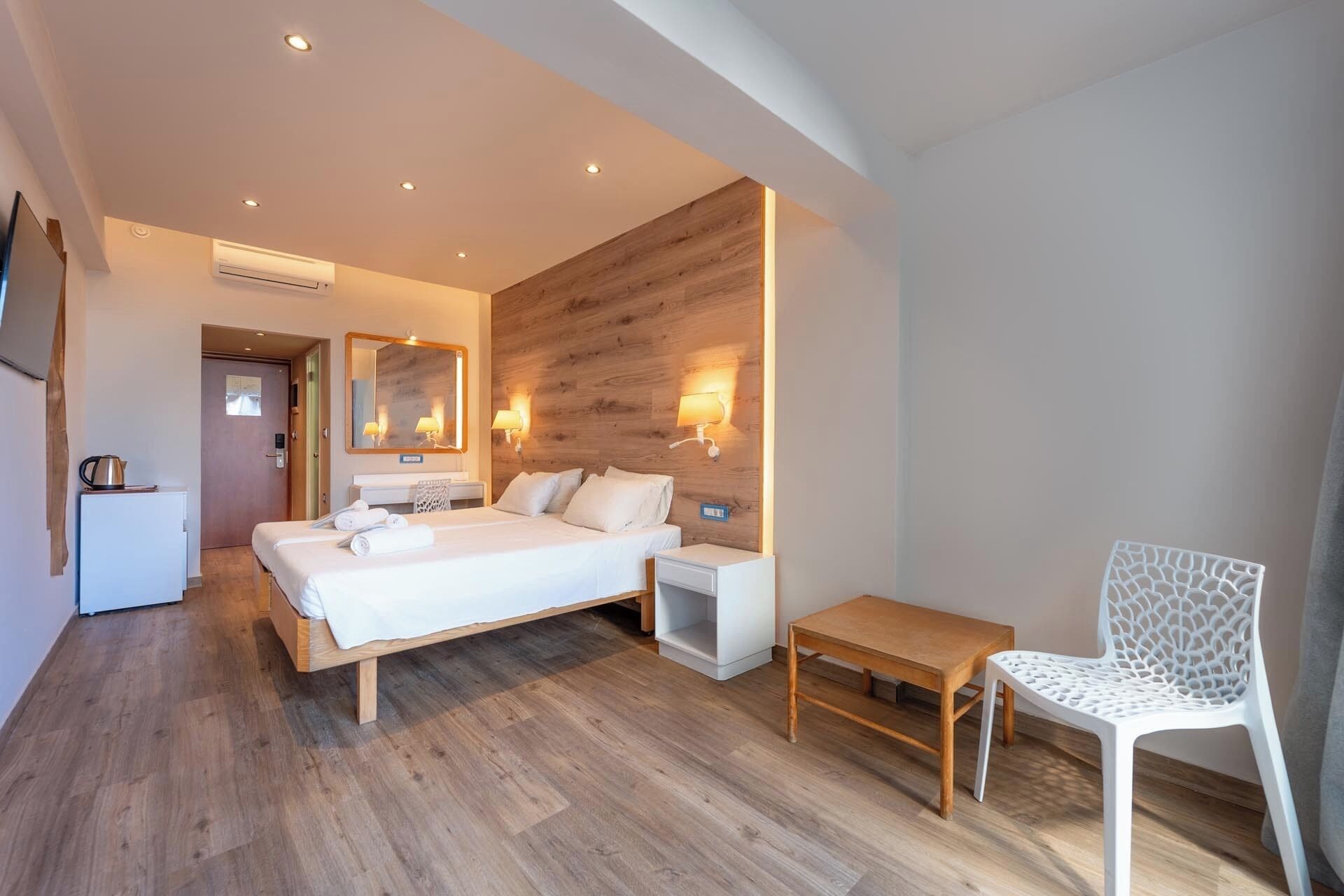 A modern hotel room with a wooden floor, a large bed, a bedside table, a chair, and a small table.