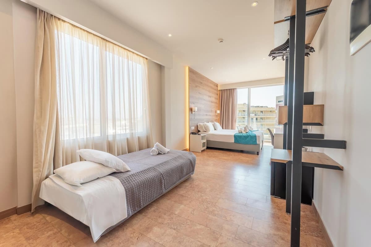 A hotel room with a large bed, a smaller bed, a desk, and a balcony with a view of the city.