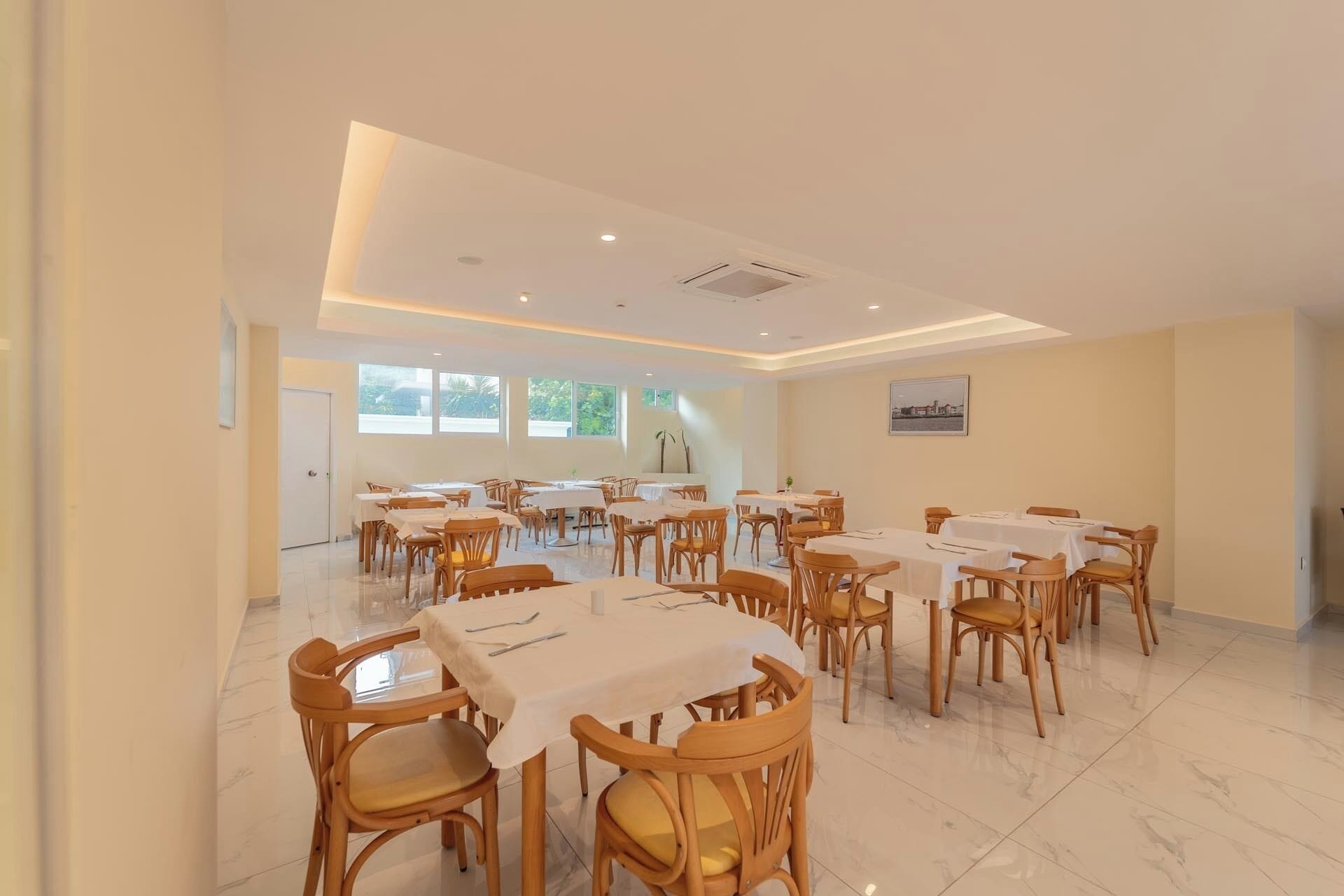 Un vaste espace dédié à la salle à manger, avec de nombreuses tables et chaises, de grandes fenêtres laissant entrer la lumière naturelle et un design épuré et moderne.