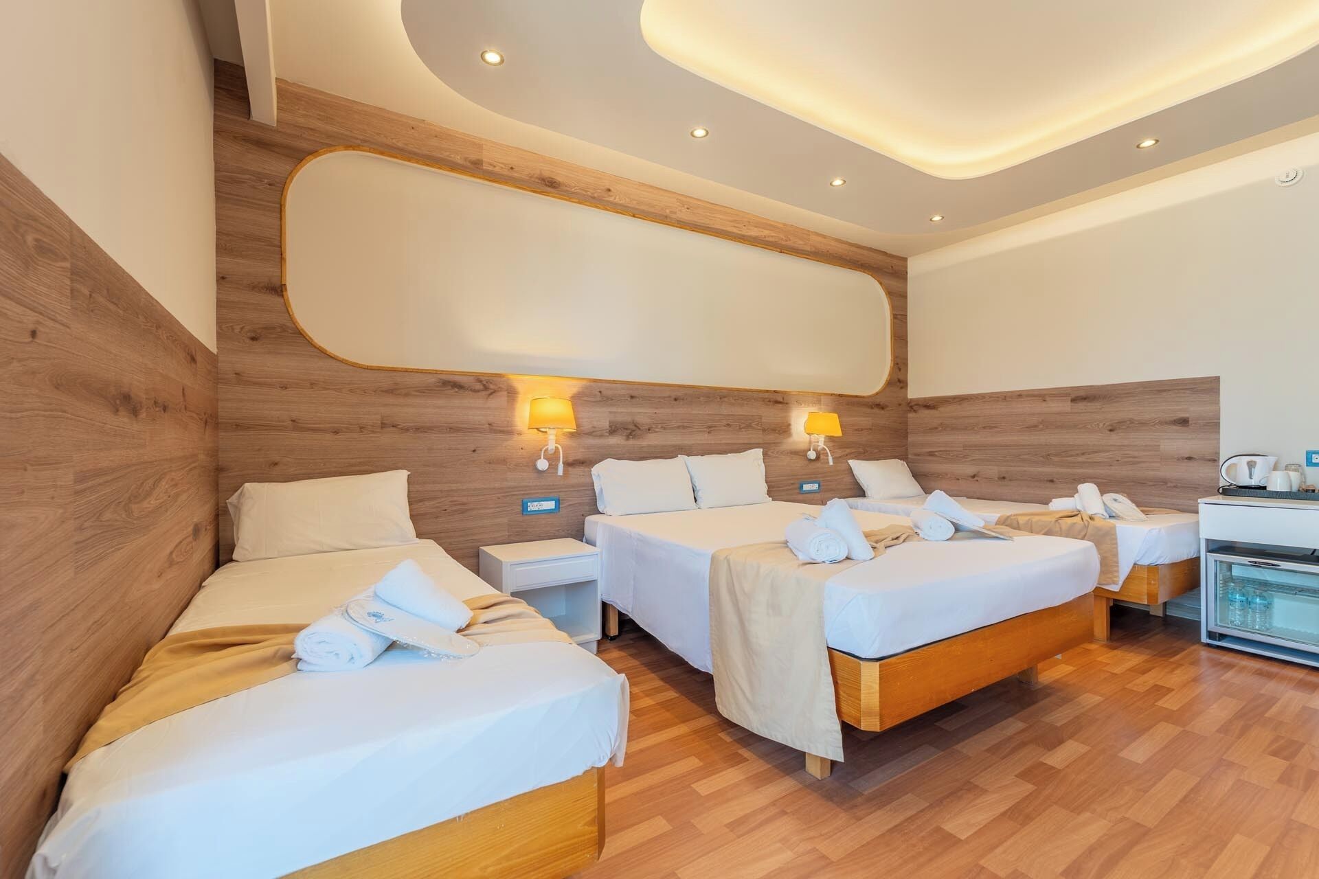 Una camera d'albergo con tre letti, poggiatesta in legno e un minibar.