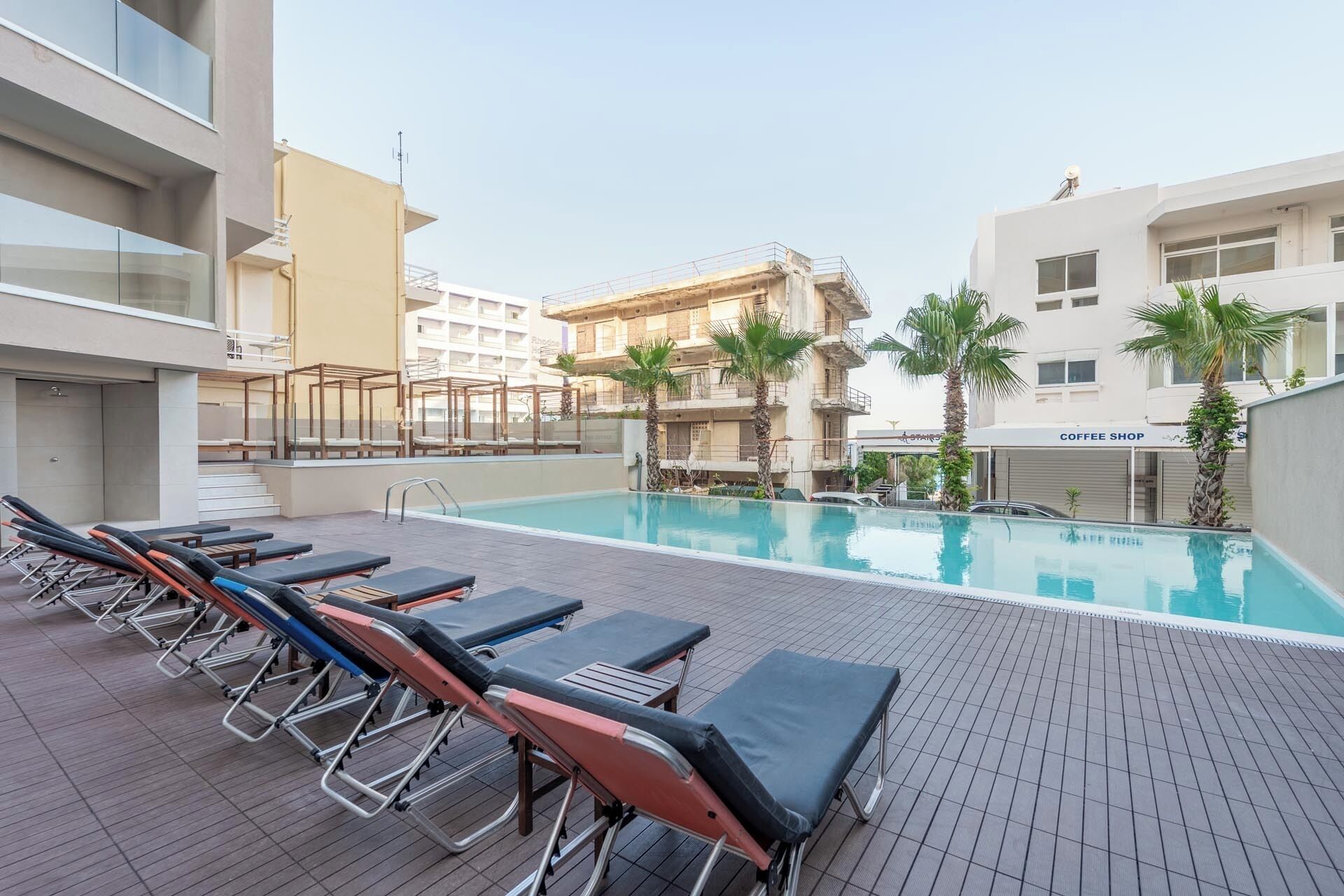 A rooftop pool with lounge chairs, a coffee shop, and a view of surrounding buildings.