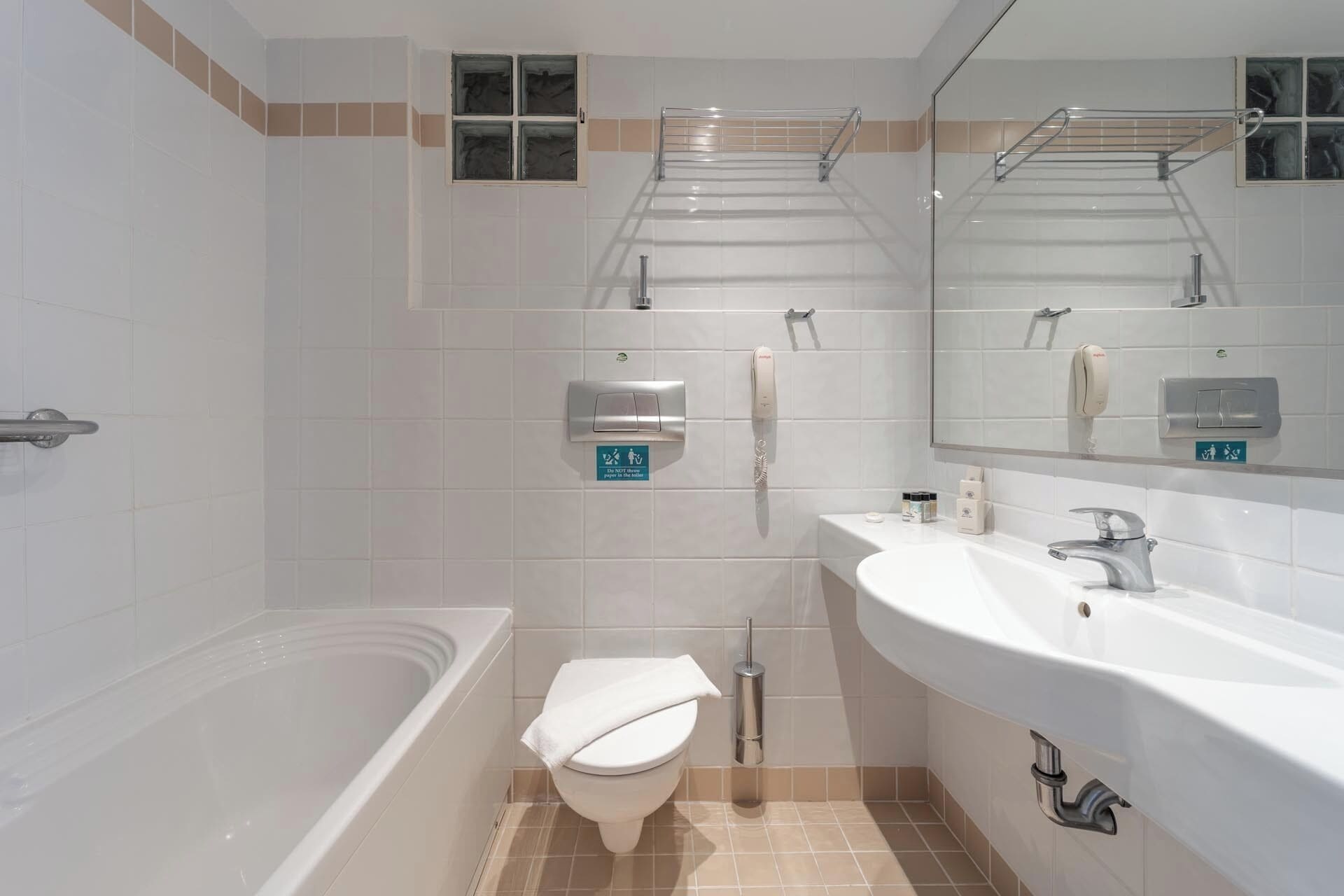 A modern bathroom with a bathtub, toilet, and sink. There are hand dryers and a soap dispenser on the wall.