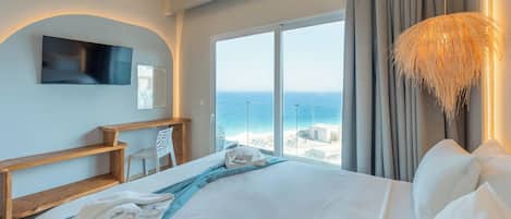 Ein Hotelzimmer mit einem großen Bett, einem an der Wand befestigten Fernseher, Meerblick und einem Balkon mit Geländer.