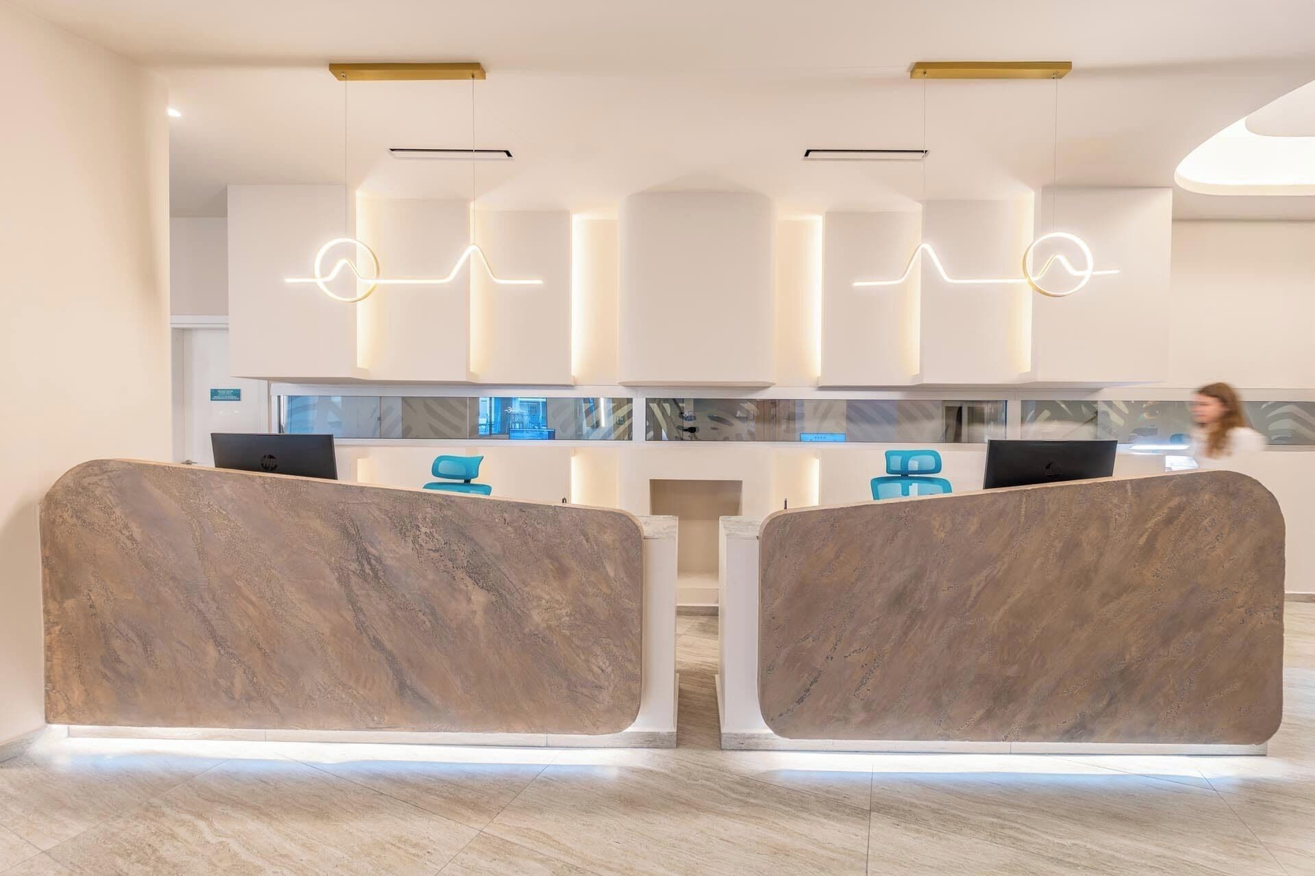 A reception area with a modern design, featuring a marble reception desk, a glass partition, and a visible office space with computers.