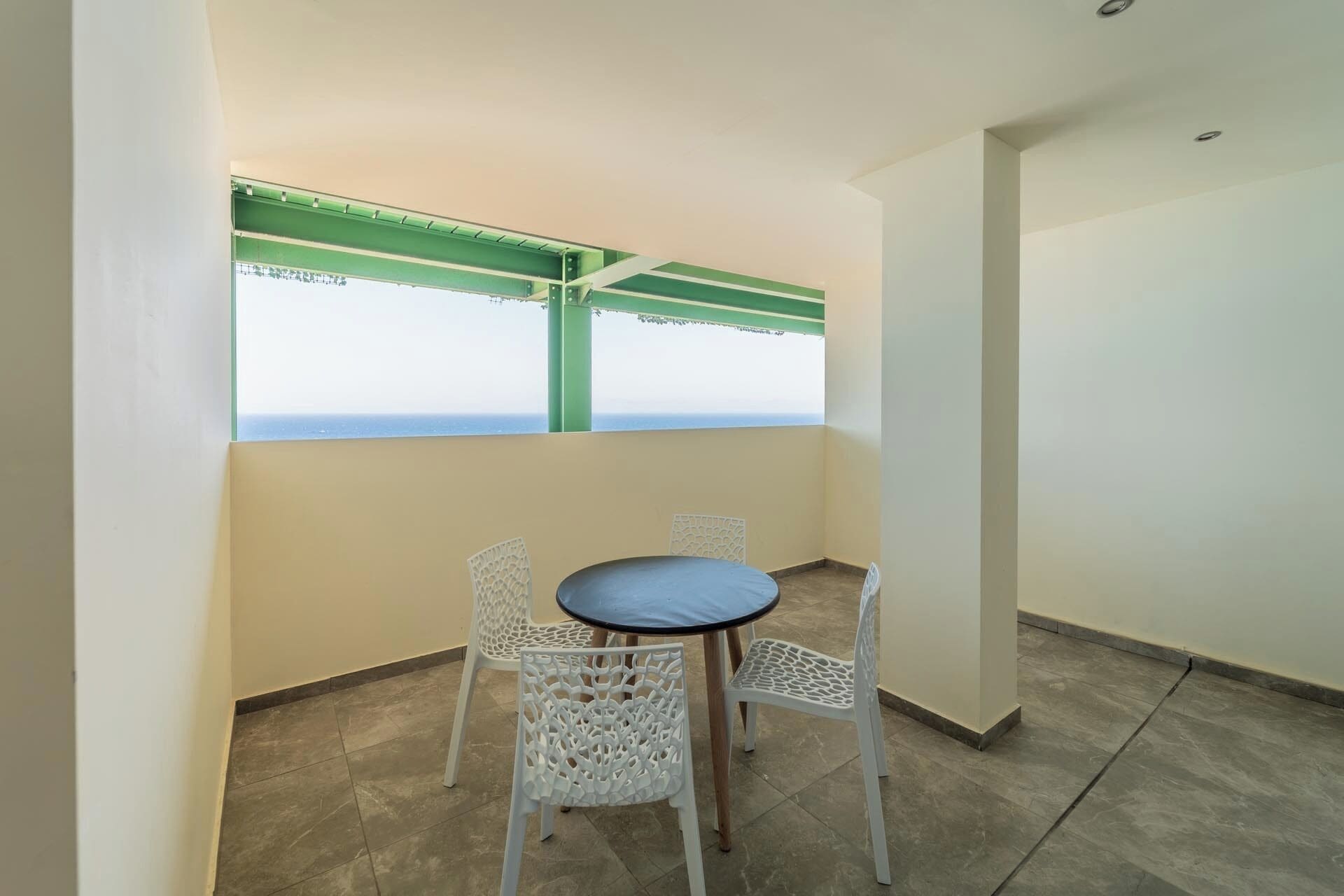 A balcony with a table and chairs, a view of the sea, and a green metal structure.