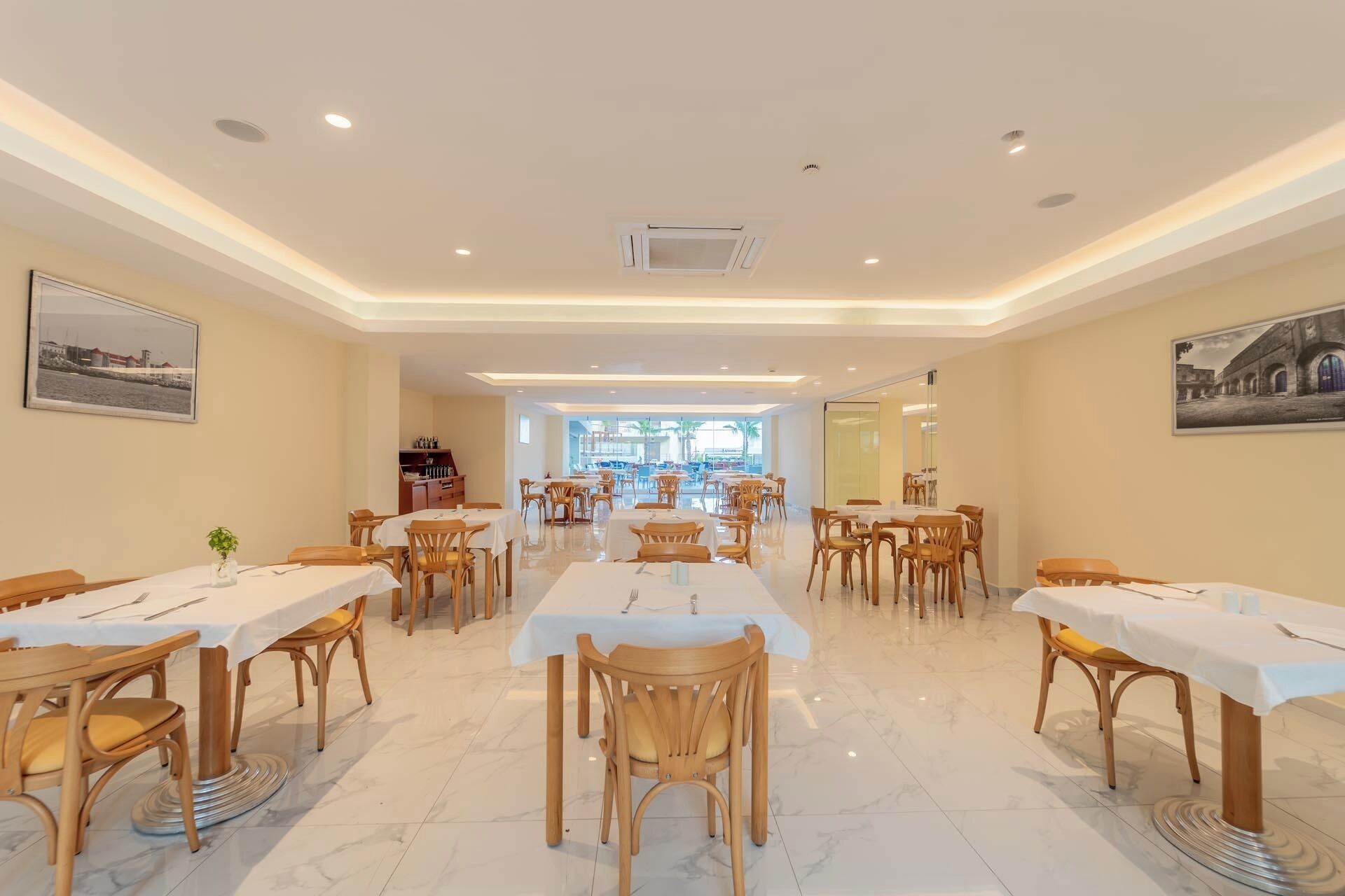 Un comedor amplio con varias mesas y sillas, vista al exterior a través de grandes ventanales y un diseño de techo moderno.