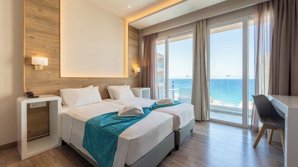 Habitación de hotel con dos camas, un escritorio y vista al océano.